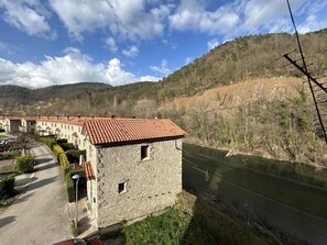 A stone building with a red-tiled roof, a paved path, and a river. - Cal Botey Apartment with Mountain Views, Wi-Fi, and Air Conditioning (Ripoll)