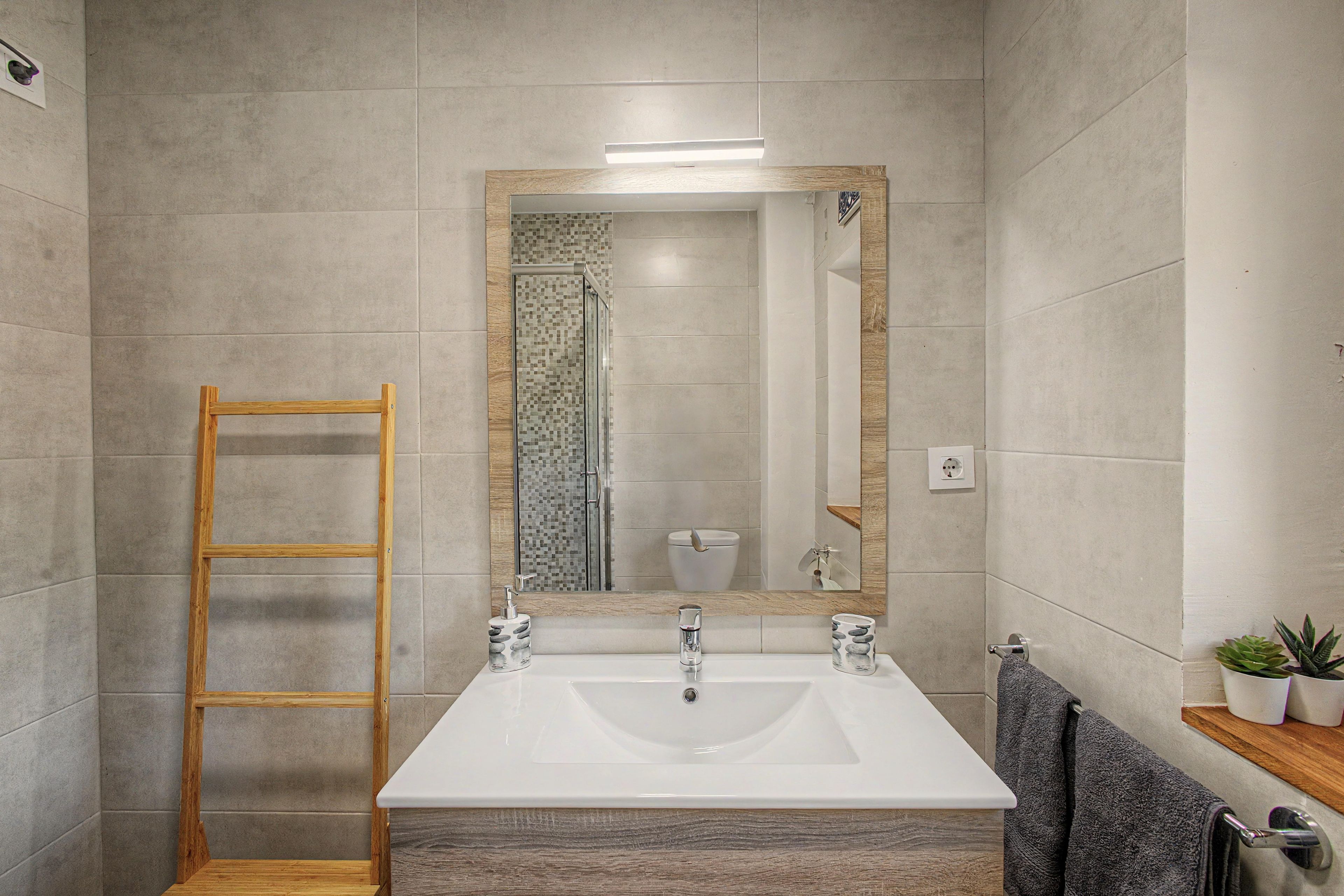 Un baño con un lavamanos grande, un espejo, una ducha y una escalera de madera.