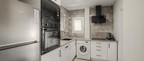 A compact kitchen with a built-in oven, a washing machine, and a microwave.