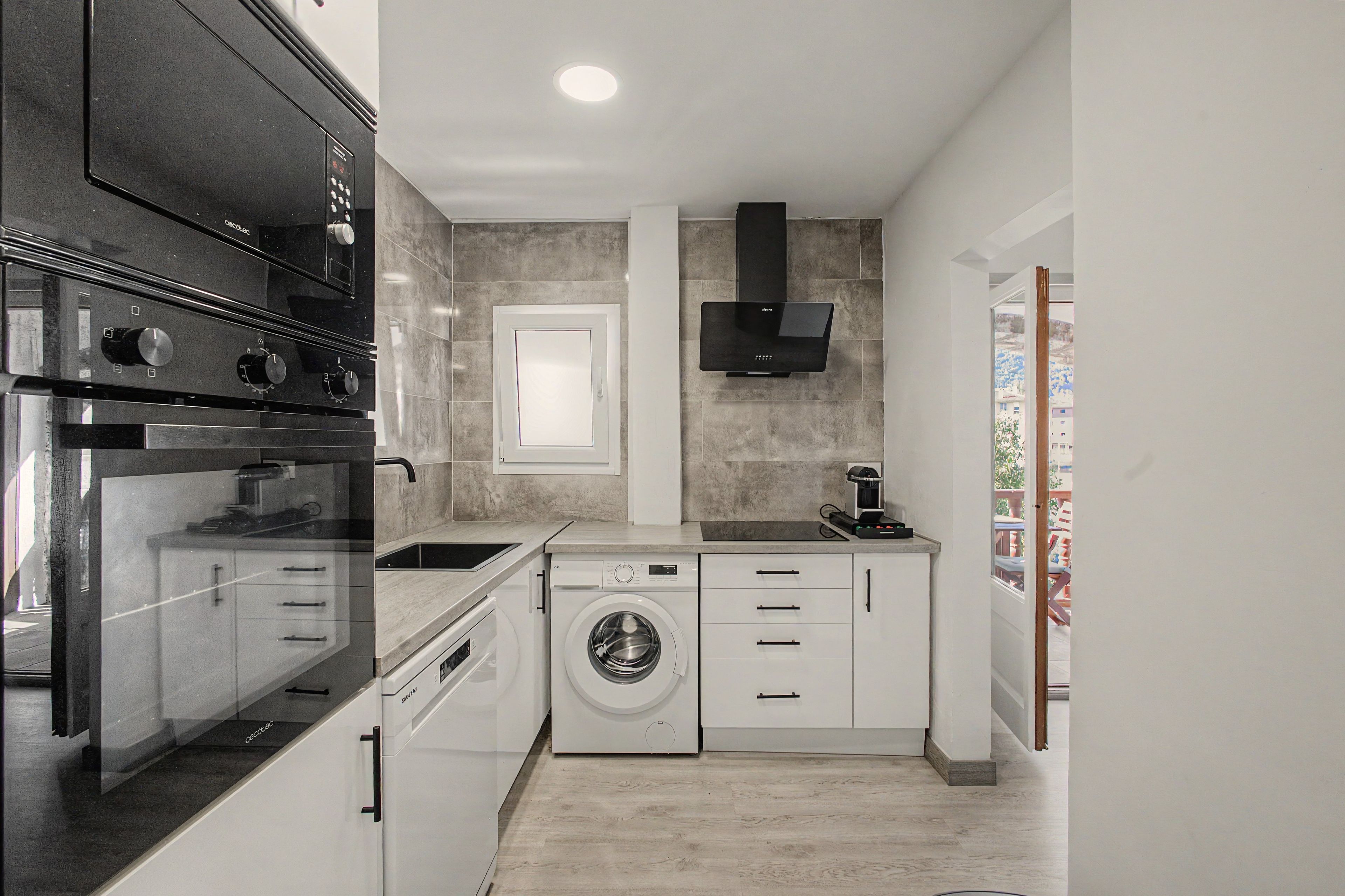 A compact kitchen with a built-in oven, a washing machine, and a coffee machine.