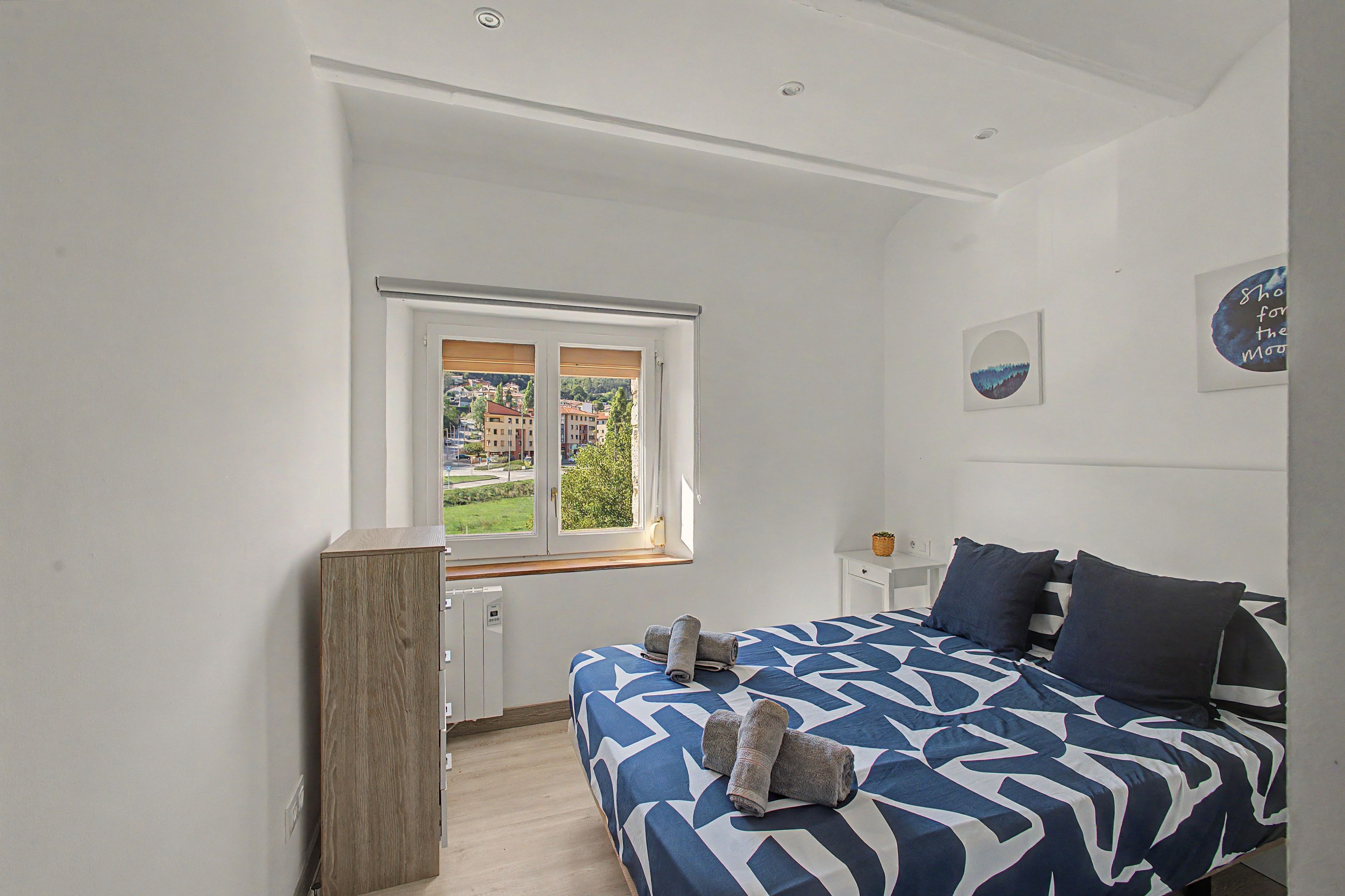 Una camera da letto con un letto, una finestra, un'opera d'arte appesa al muro e un armadietto in legno.