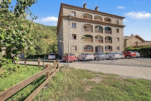 A stone building with multiple balconies and parked cars in front.