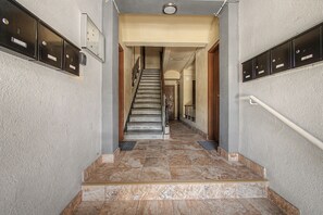 A hallway with a staircase leading to another floor, featuring a handrail, a door at the bottom, and mailboxes on either side.