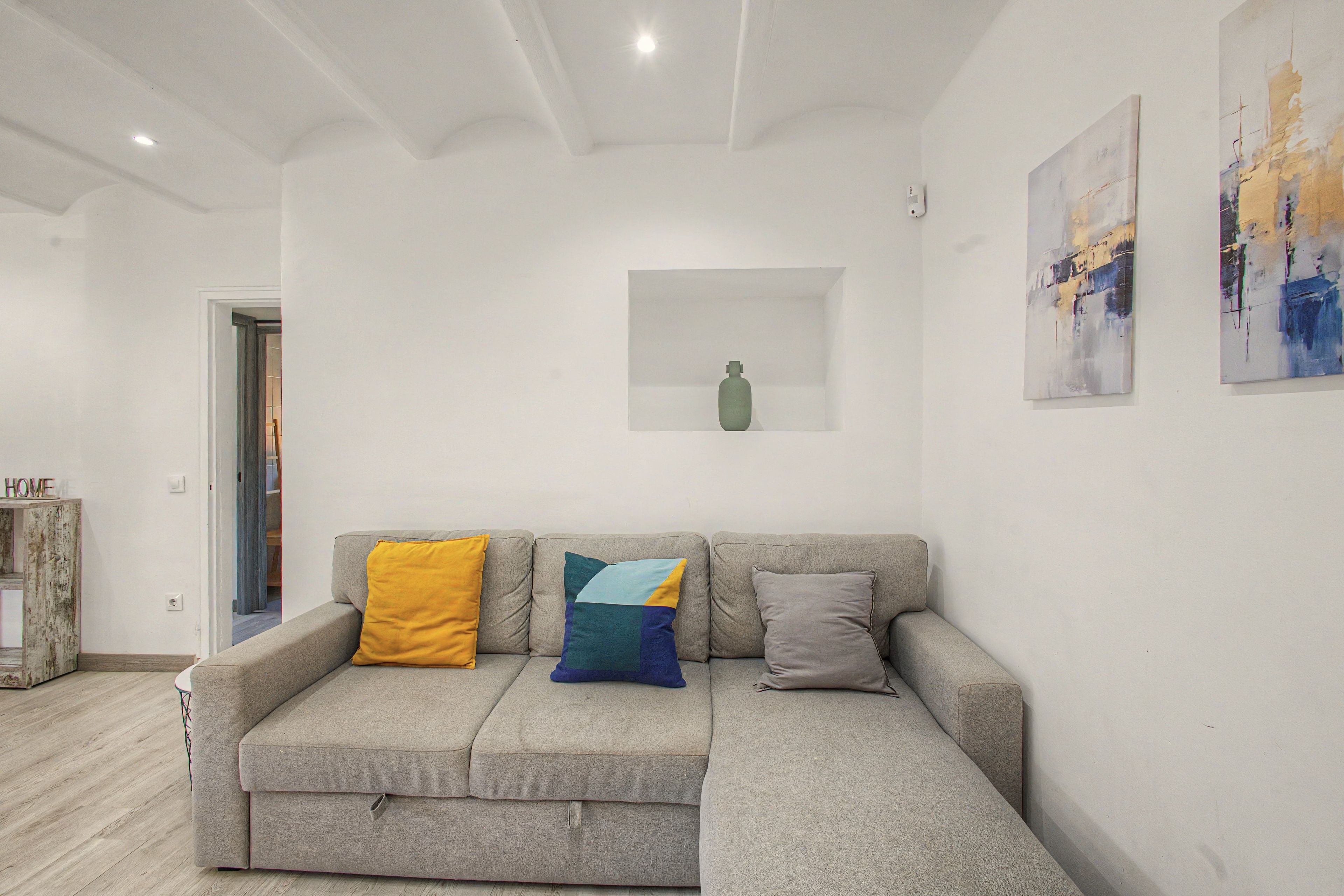 Un salón en tonos neutros con un sofá gris, un estante pequeño blanco y arte abstracto en las paredes.