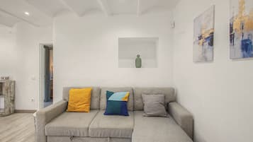 Un salón en tonos neutros con un sofá gris, un estante pequeño blanco y arte abstracto en las paredes.