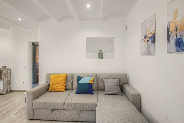 A neutral-toned living room with a grey sofa, a small white shelf, and abstract art on the walls.