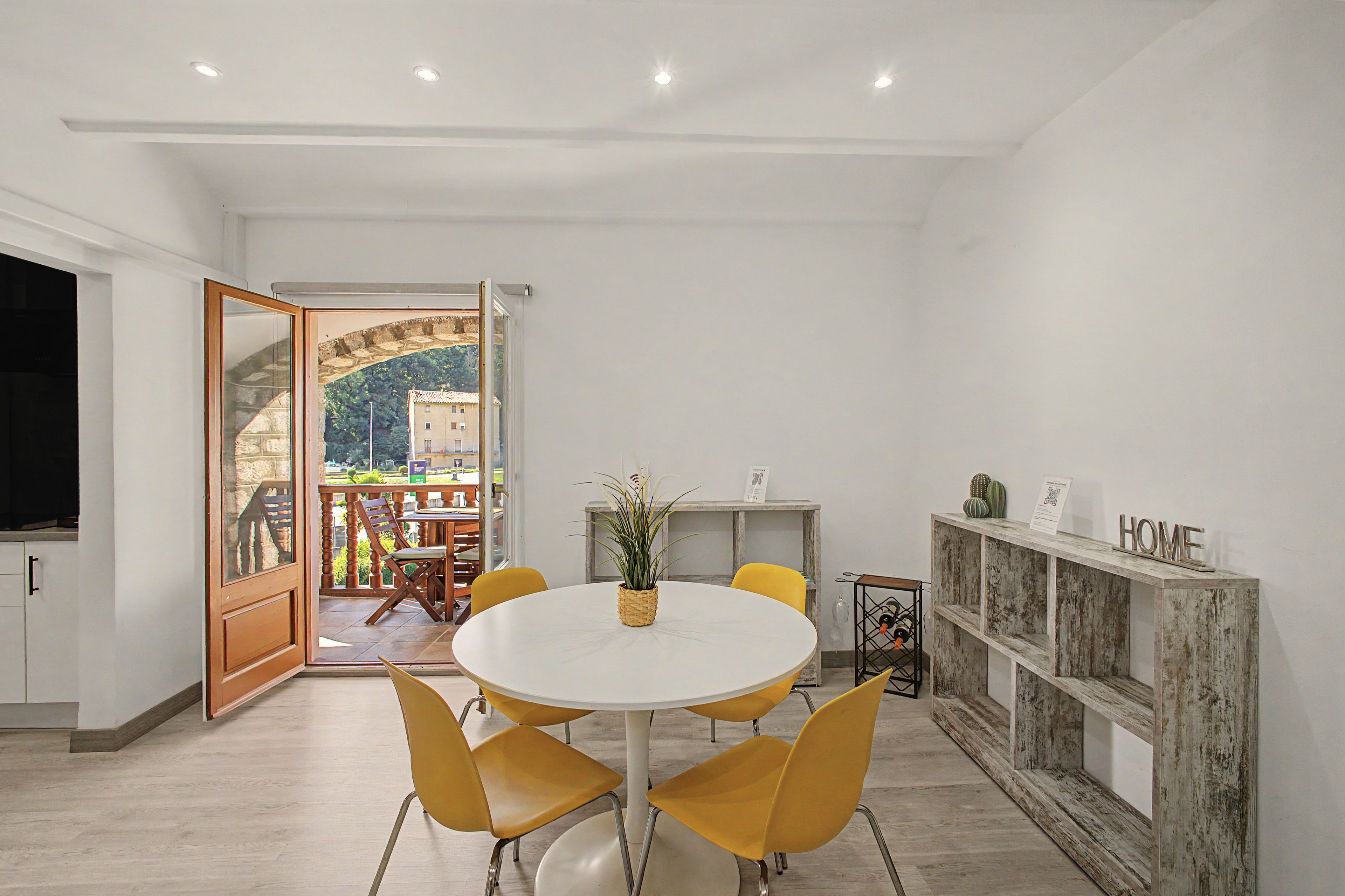 Un comedor moderno con una mesa redonda, sillas amarillas y vistas a una terraza exterior a través de un ventanal.