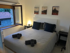 Un lit bien fait, avec des oreillers, une table de chevet sur laquelle se trouve une lampe, et trois tableaux accrochés au mur.