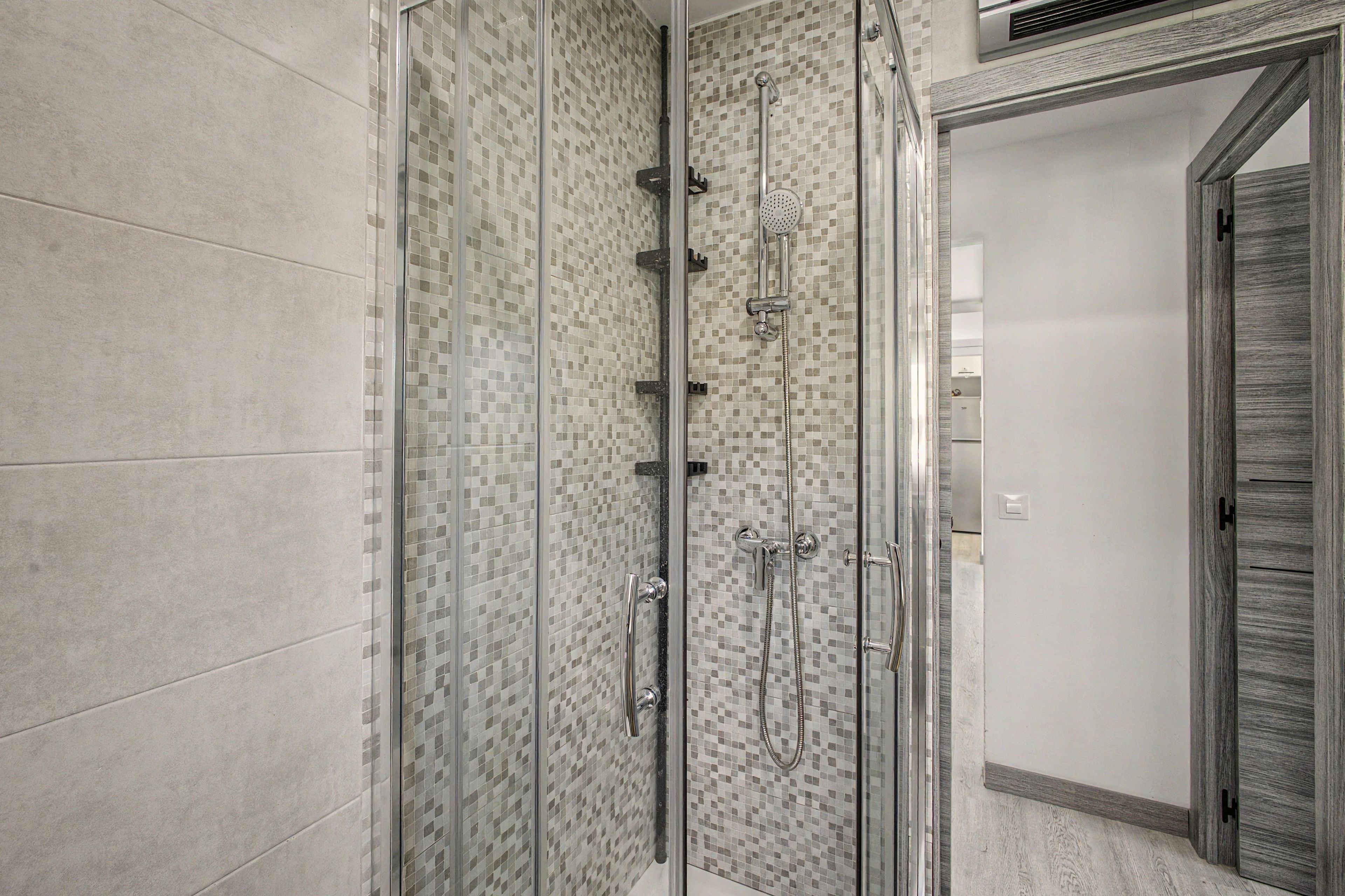 Ducha a nivel con puerta de vidrio y pared de mosaico de azulejos.