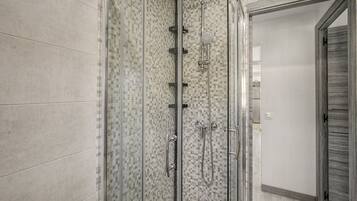Ducha a nivel con puerta de vidrio y pared de mosaico de azulejos.