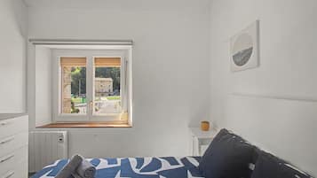 Ein Schlafzimmer mit einem Bett, einem Fenster, einem Heizkörper und einem kleinen Nachttisch.