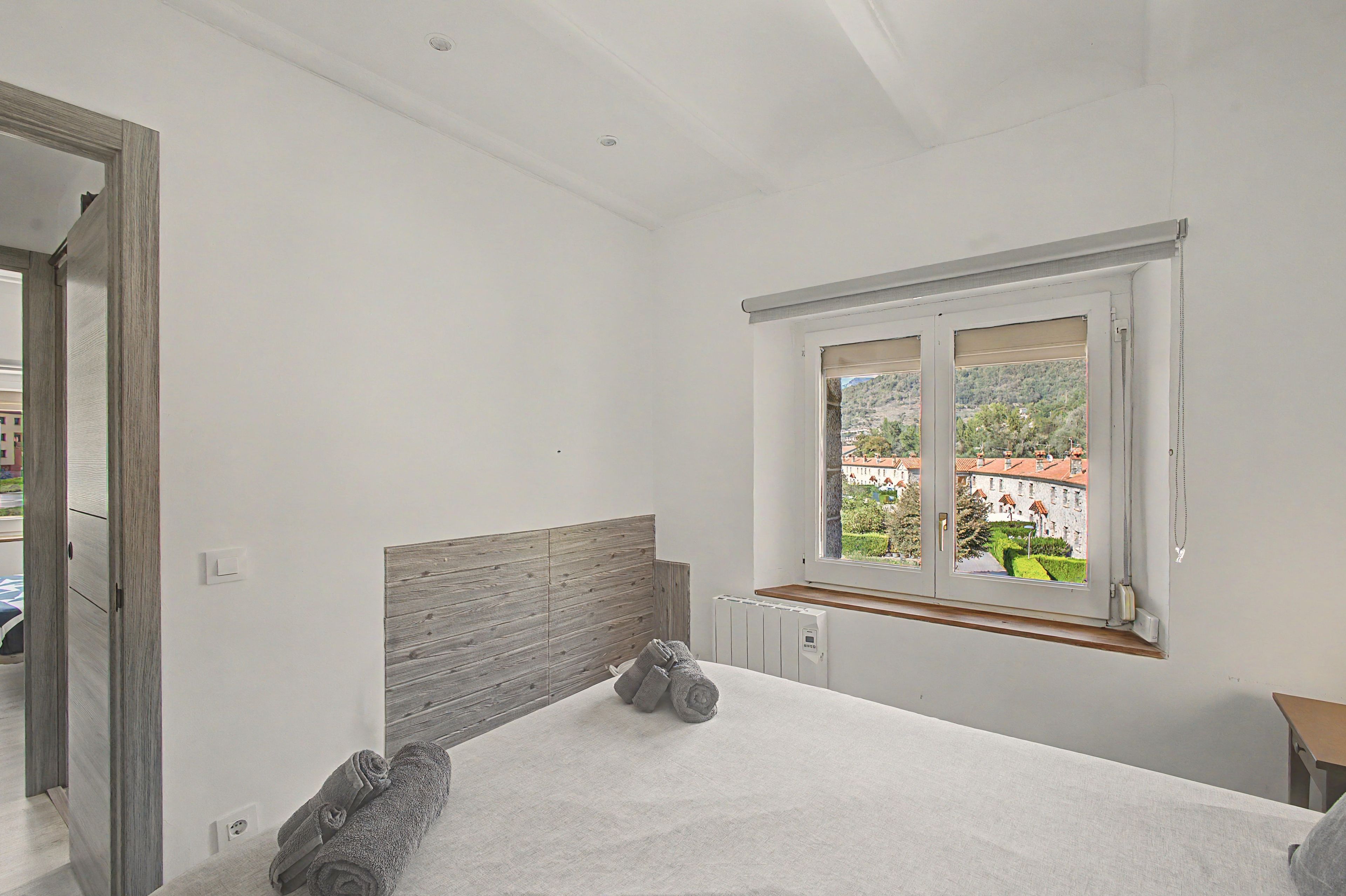 A bedroom with a large window, a radiator, and a neatly made bed.