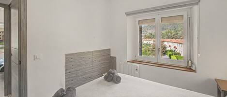 A bedroom with a large window, a radiator, and a neatly made bed.