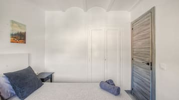 Ein Schlafzimmer mit einem Bett, einem Nachttisch, einer Tür und einem an der Wand hängenden Bild.