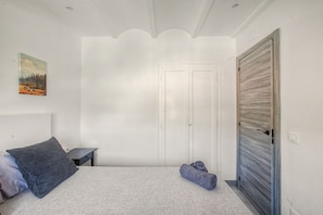 Una camera da letto con un letto, un comodino, una porta e un quadro appeso al muro.