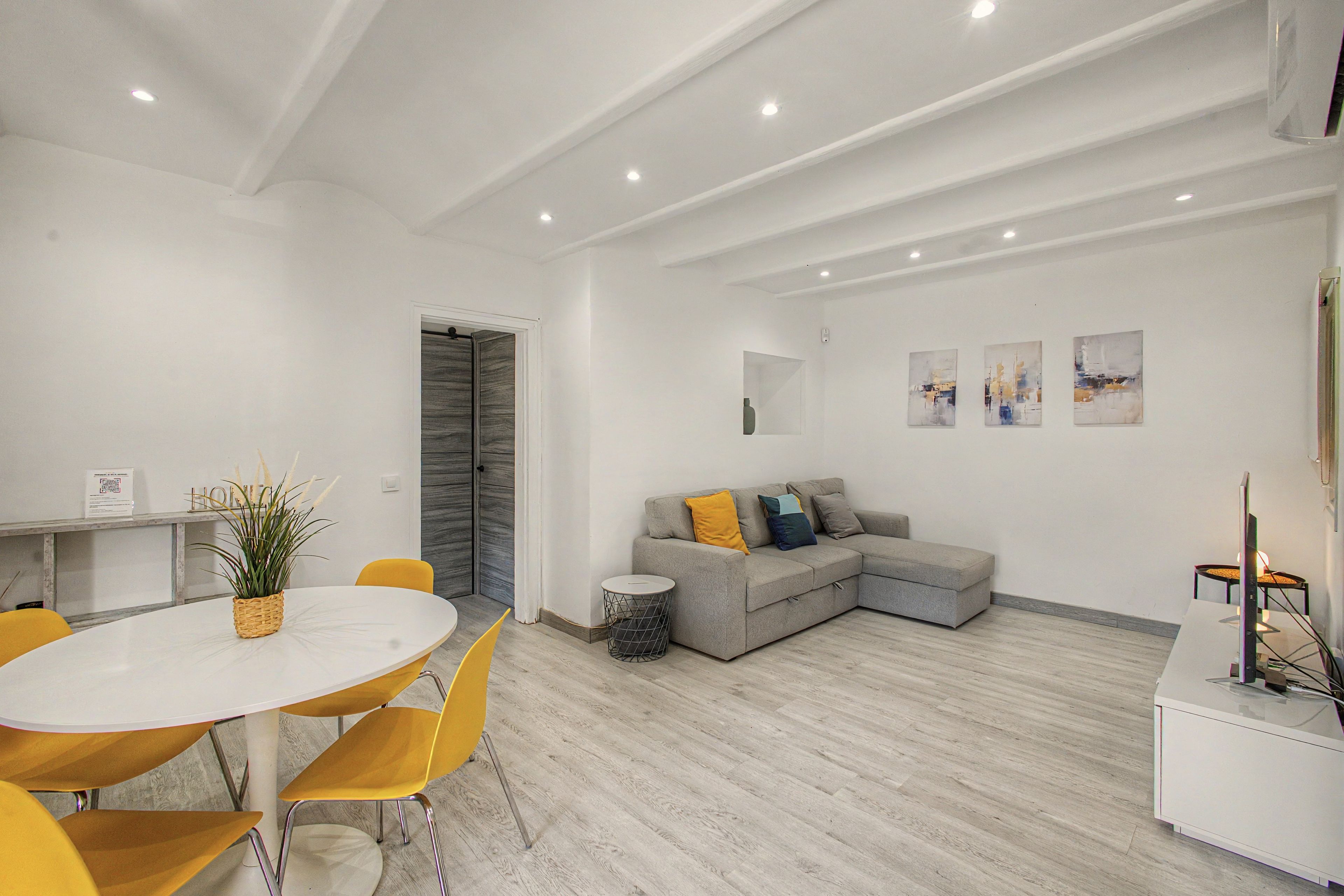 Un espace de vie moderne comprenant un coin repas, un canapé d’angle gris et une table ronde blanche avec des chaises jaunes.