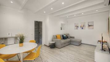 Un espace de vie moderne comprenant un coin repas, un canapé d’angle gris et une table ronde blanche avec des chaises jaunes.