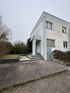 En moderne bygning med to etager, fladt tag, overdækket indgang med trapper og et lille haveområde.