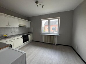 Et køkken med hvide skabe, indbygget ovn, et vindue og en radiator.