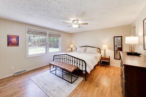 Ein Schlafzimmer mit einem Bett, einer Bank, einem Deckenventilator, zwei Nachttischlampen, einem Fenster und einem Spiegel.