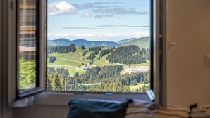 Ein Zimmer mit großem Fenster und Blick auf eine grüne Landschaft mit Bäumen und Hügeln.