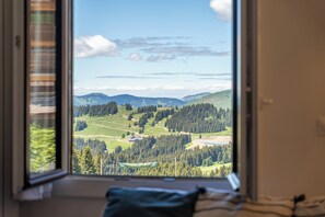 A room with a large window offering a view of a green landscape with trees and hills. - Neva- L'Écrin de la Falaise - Avoriaz (Morzine)
