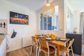 A dining area with a table set for four, a hanging light fixture, and a cityscape painting on the wall. - Neva- L'Écrin de la Falaise - Avoriaz (Morzine)