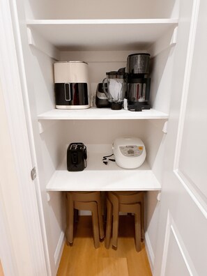 Eine Küche mit Kaffeemaschine, Mixer, Toaster und einem kleinen Tisch mit Stühlen.
