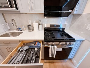 A modern kitchen with a stainless steel stove, white cabinets, and a drawer organizer with utensils. - Cozy 2-bedroom house No Living room (San Gabriel)