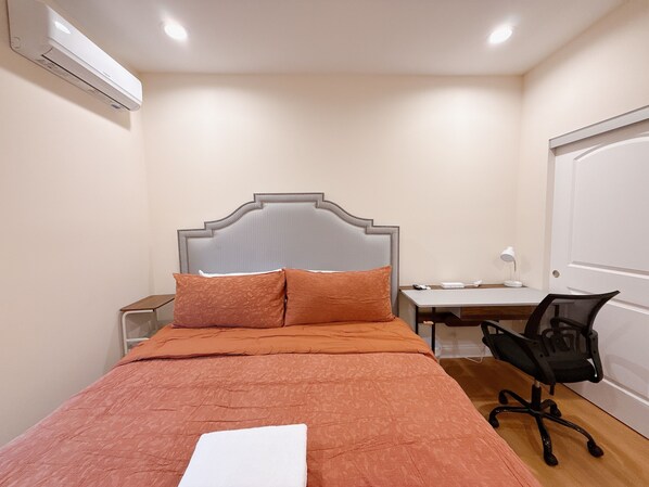 Ein Schlafzimmer mit einem Bett, einem Schreibtisch, einem Stuhl und einer Klimaanlage.