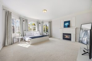 Ein Schlafzimmer mit Bett, Kamin, Fernseher und großen Fenstern.