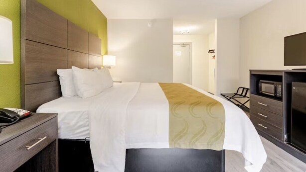 Ein Hotelzimmer mit Bett, Nachttisch, Lampe, Fernseher und Mikrowelle.