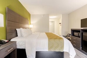 Habitación de hotel con cama, mesita de noche, lámpara, televisor y microondas.