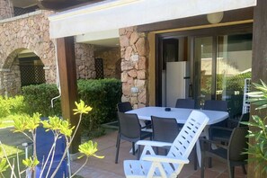 Eine Terrasse im Freien mit einer Steinsäule, einer überdachten Sitzgelegenheit und einer Glastür zum Innenbereich.