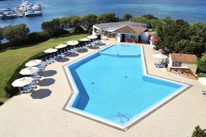 Ein Schwimmbecken mit Liegestühlen und Sonnenschirmen, ein kleines Gebäude und Boote im Hintergrund.