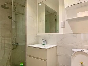 Ein Badezimmer mit einer gläsernen Duschkabine, einem weißen Waschbecken mit Spiegel darüber und einer Toilette mit Deckel.