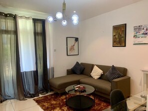 Ein Wohnzimmer mit einer Couch, einem Couchtisch, einem Glastisch, einer Chandelier, Vorhängen und Wandbildern.
