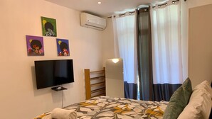Et soveværelse med seng, fladskærms-tv, aircondition, gardiner og billedkunst på væggen.