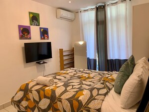 Ein Schlafzimmer mit Bett, Flachbildfernseher, Klimaanlage, Vorhängen und Wandbildern.