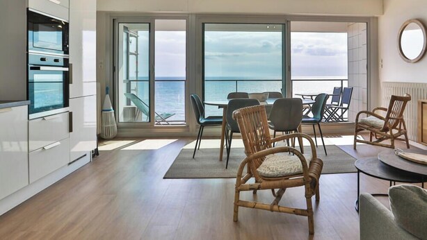 A modern kitchen with built-in appliances, a dining area with wicker chairs, and a balcony with a view of the sea. - Brasilia - Vue mer d’exception aux Sables, balcon & plage (Les Sables-d´Olonne)