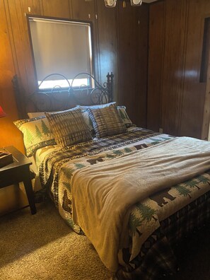 Ein Schlafzimmer mit einem Bett, einem Nachttisch, einem Fenster und Holzwänden.