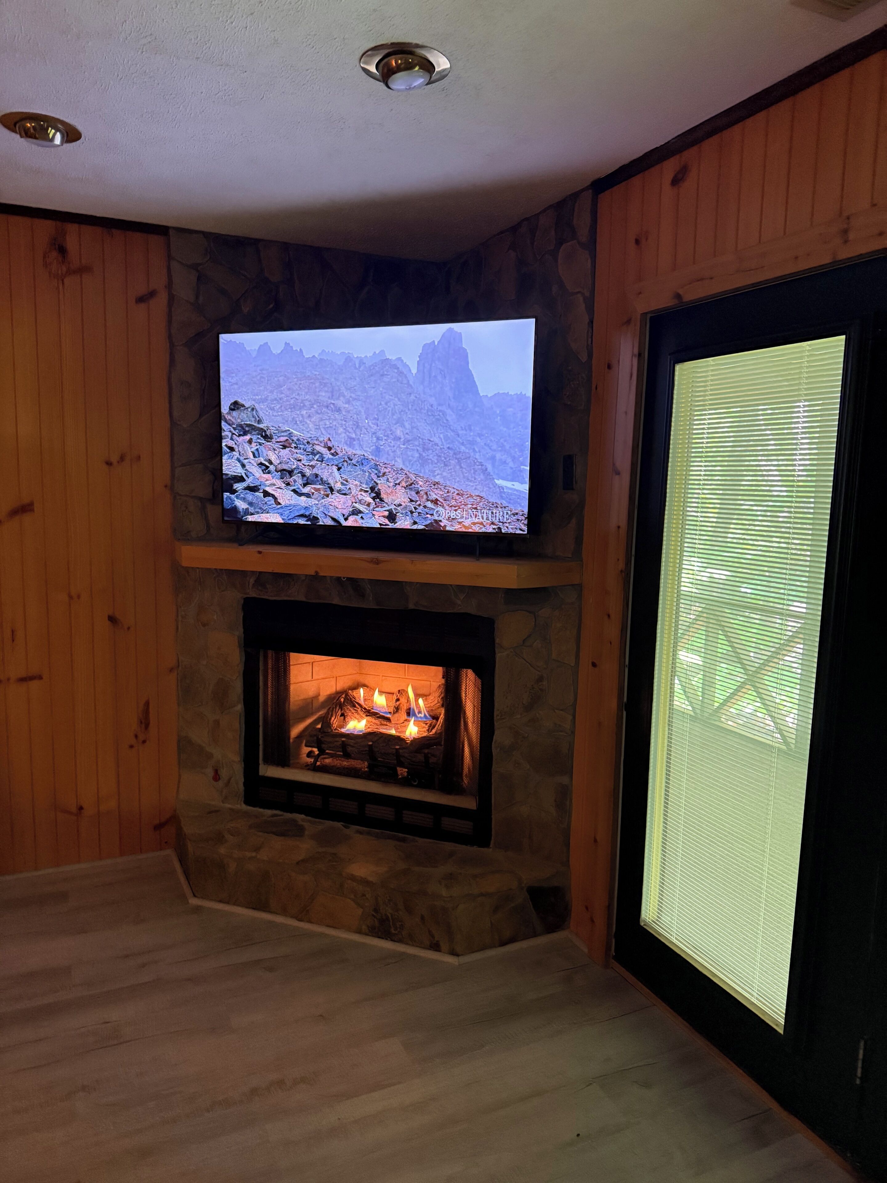 A living room with a stone fireplace, a flat-screen TV mounted above it, and a sliding glass door.