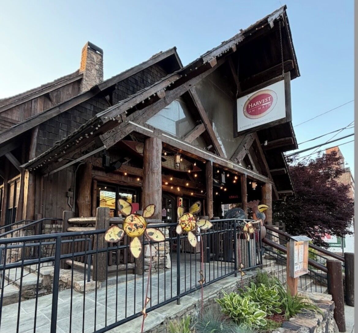 A rustic building with a wooden facade, a sign reading 'HARVEST ON MAIN ST.', and a metal fence in front.