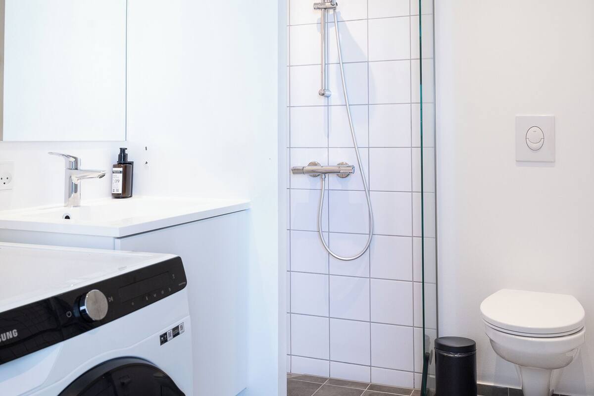 A modern bathroom with a washing machine, a glass shower enclosure, and a toilet.