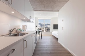 A modern kitchen with a large window, a dining area, and a bed. - Aurora City Apartments (Nuuk)