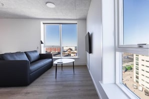 Ein modernes Wohnzimmer mit einer schwarzen Ledersofa, einem kleinen runden Tisch und einem großen Fenster mit Blick auf die Stadt.