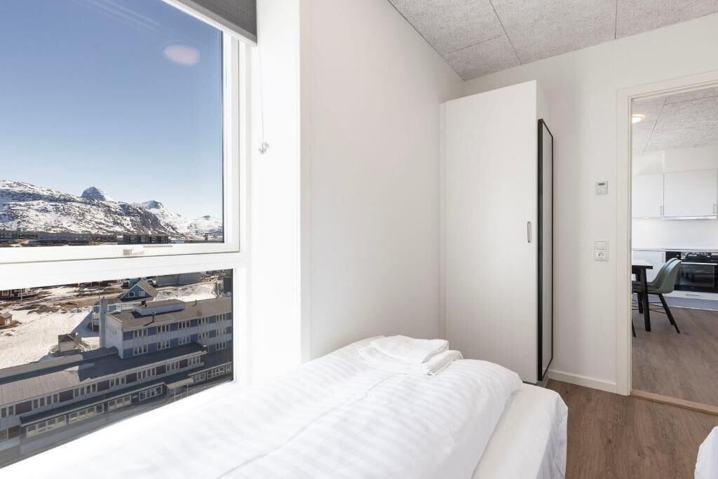 Ett sovrum med en säng, ett fönster med utsikt över ett snötäckt landskap, en dörr och en liten arbetsplats med ett skrivbord.