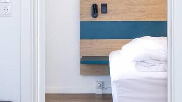 A bedroom with a bed, a bedside table, a nightstand, and a wall-mounted phone.