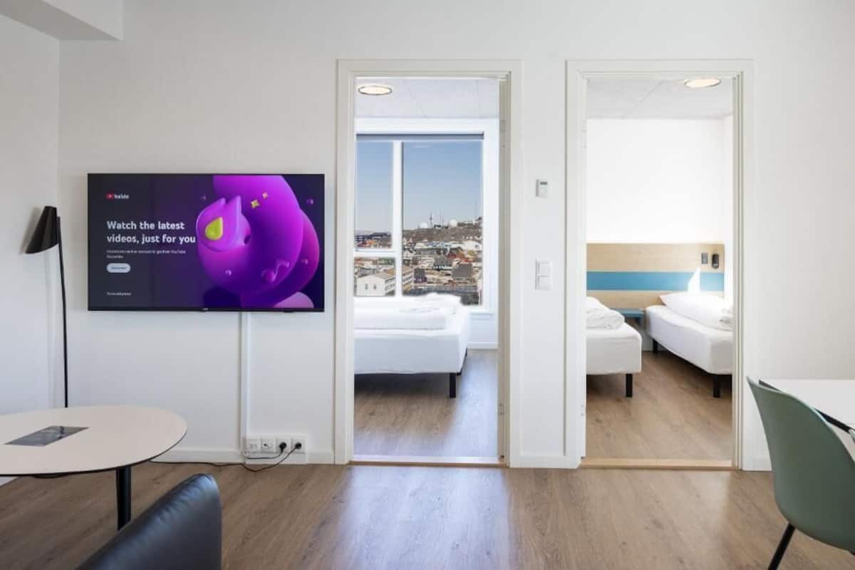 Ett modernt hotellrum med en stor TV, en balkong med utsikt över staden, ett litet bord och en stol.