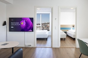 Ein modernes Hotelzimmer mit großem Fernseher, einem Balkon mit Blick auf die Stadt, einem kleinen Tisch und einem Stuhl.